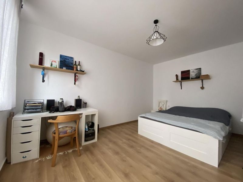 A bright room with a wood-decor floor, a desk, and a bed in a studio apartment.