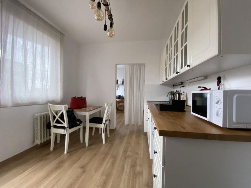 White kitchen with wood-patterned flooring, table, and chairs in a studio apartment.