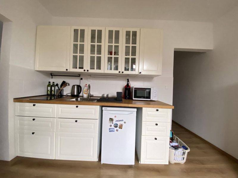 A kitchen in a studio apartment with a wood-patterned floor and white furniture.
