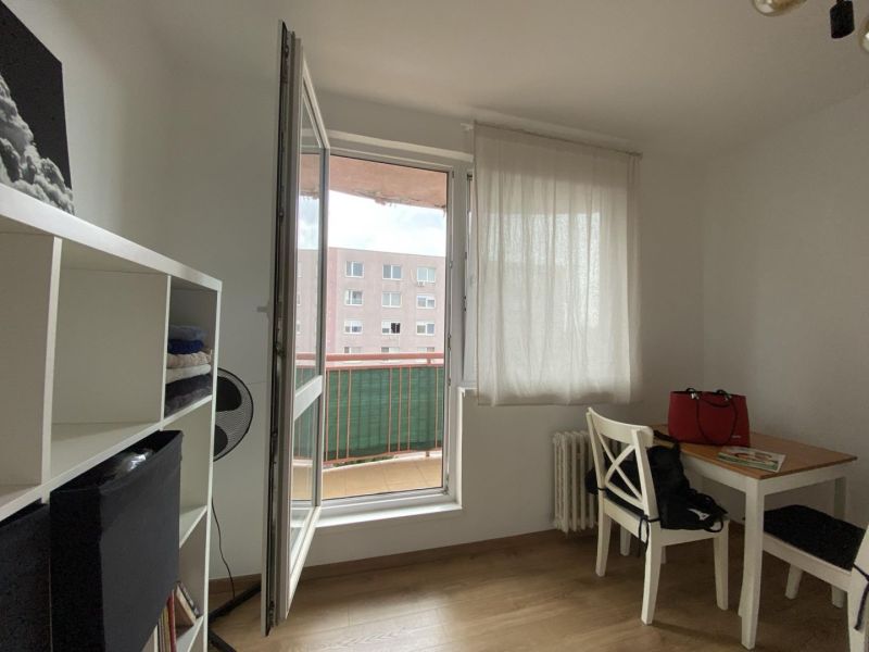 A one-room apartment with a wooden decor floor, a table, chairs, and a shelf by the window.