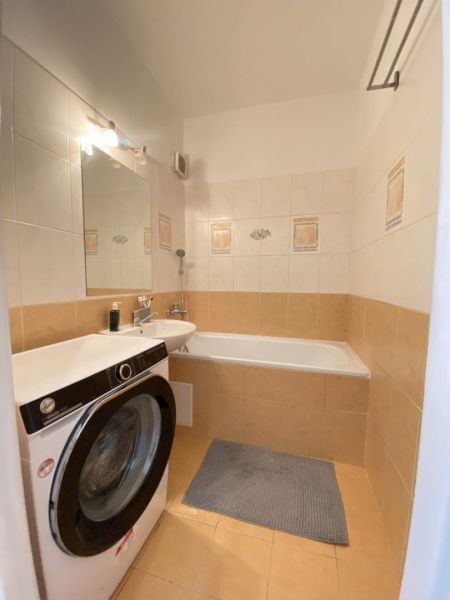 Bathroom with a bathtub and a washing machine in a studio apartment, light tiles and a mirror.