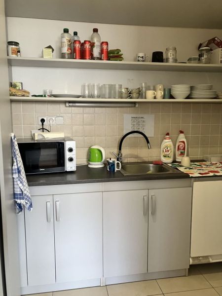 Kitchenette in commercial premises with a microwave, dishes, and shelves with drinks.
