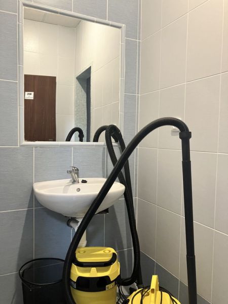 Interior of commercial premises with a sink, mirror, and vacuum cleaner in the room.