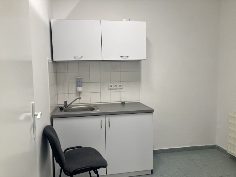 A sink with a white cabinet and a chair in commercial premises.