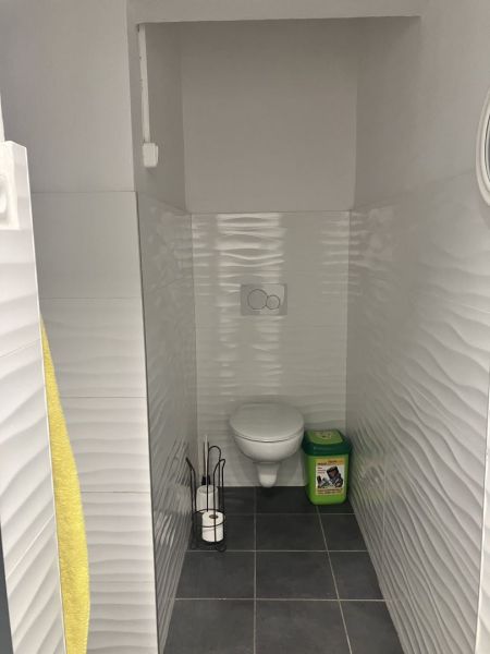 Bathroom with toilet, tiled floor, and white embossed walls.