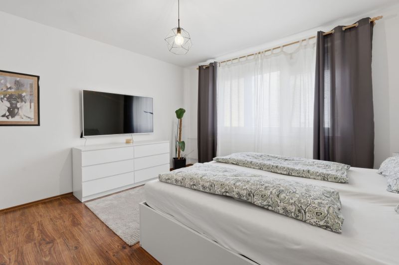 Bedroom in a 3-room apartment with a wood-decor floor, a television, and a dresser.