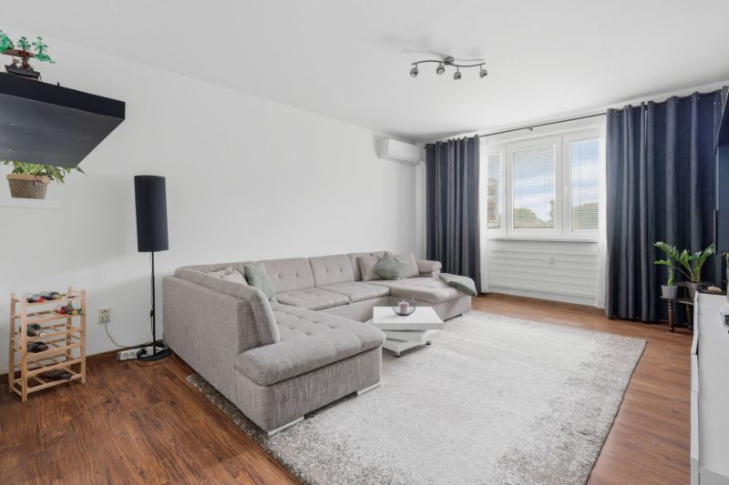 A bright living room with a corner sofa, wood-patterned flooring, 3-room apartment.