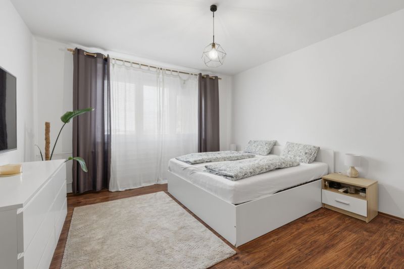 A bright bedroom with a double bed, wardrobe, wood-patterned flooring, and subtle lighting in a 3-room apartment.