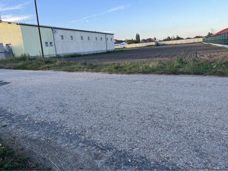 Road and adjacent residential plots in Holice, visible warehouse building.