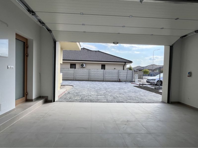 An open garage in a family house with a view of a paved yard.
