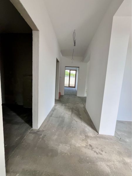 A hallway in a family house with smooth white walls and an unfinished floor.