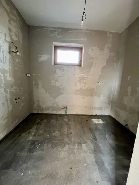 Unfinished room in a family house with a concrete floor and a small window.