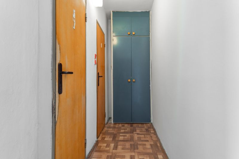 A narrow hallway in a 3-room apartment with a wooden decor floor and a built-in wardrobe.
