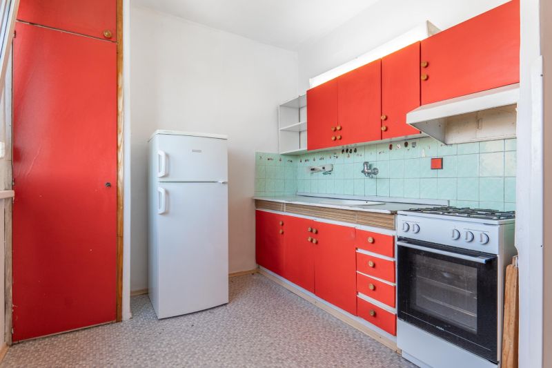 A kitchen in a 3-room apartment with red cabinets and a refrigerator.