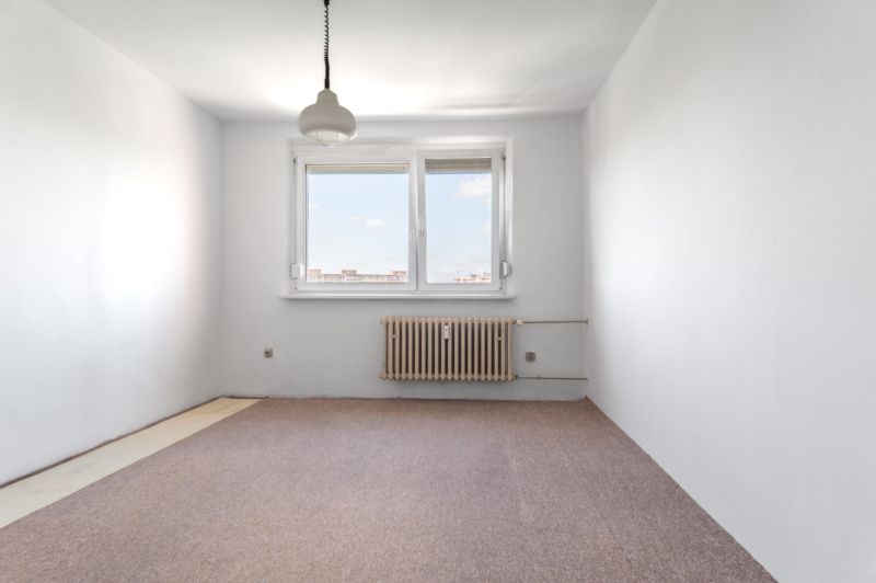 An empty room with a carpet, radiator, window, and pendant light in a 3-room apartment.