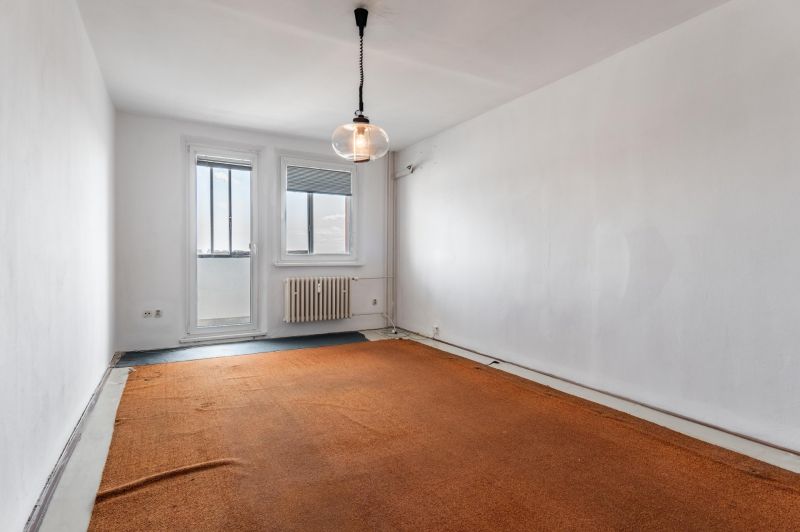 A room with an orange carpet, white wall, window, and radiator in a 3-room apartment.