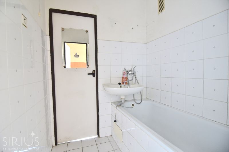 A bathroom in a 3-room apartment with simple white tiles and a bathtub.