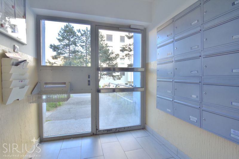 Apartment entrance with mailboxes, view of the outside walkway and trees.