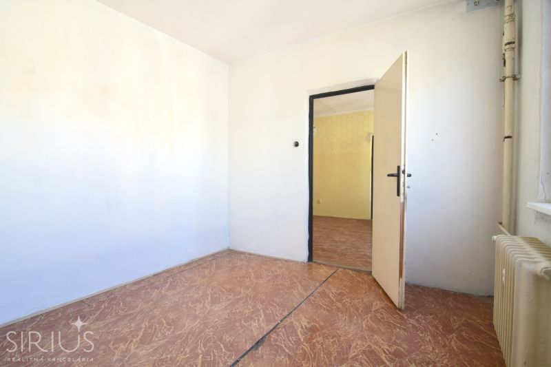 An unfurnished room in a 3-room apartment with a wooden decor floor and a radiator.