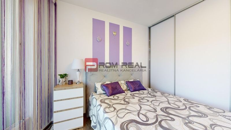 Bedroom with a bed, storage space, and decorations in a 2-room apartment with a wood-patterned floor.