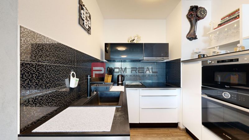 A kitchen in a 2-room apartment with dark tiles and a wooden decor floor.