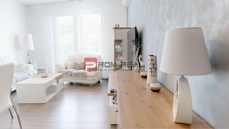 Living room in a two-room apartment with a wooden decor floor and white furniture.
