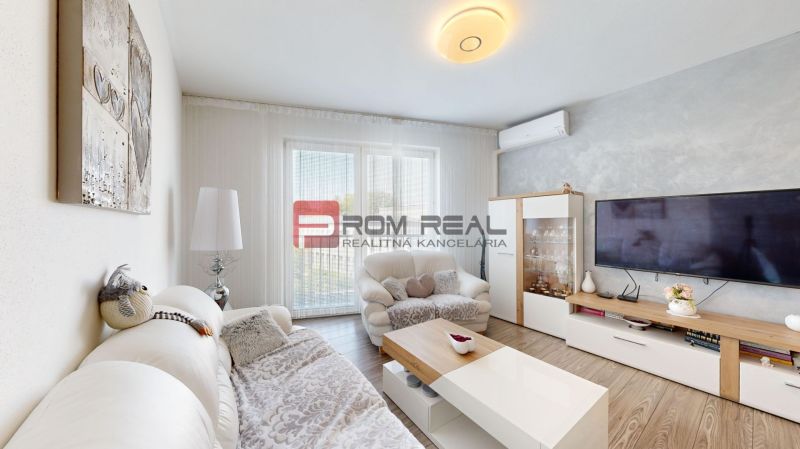 Living room in a two-room apartment with a wooden decor floor, a comfortable sofa, and a television.