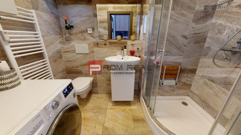 A bathroom in a 2-room apartment with a washing machine, shower, and ceramic tiles.