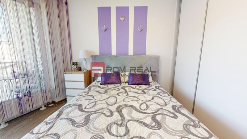 A bedroom with purple accessories, light furniture, and a wooden decor floor in a two-room apartment.