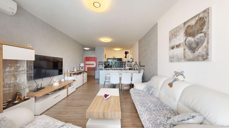 Living room in a two-room apartment with white furniture and a wooden decor floor.