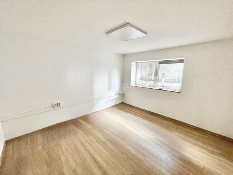 A room with a wood-patterned floor in an office, empty, with a window and white walls.