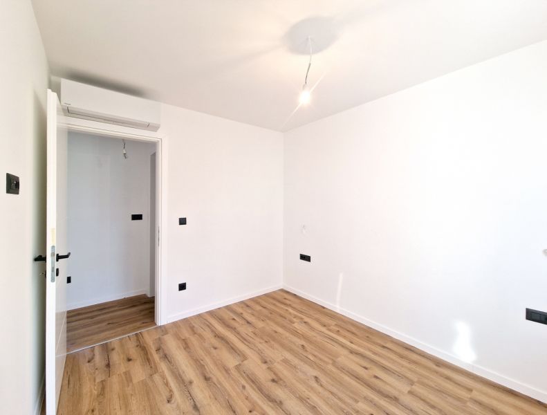 A room with white walls and a wood-decorated floor in a 3-room apartment.