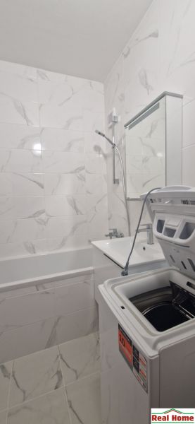 A bathroom in a 2-room apartment with a shower, bathtub, and washing machine, tiled with white tiles.