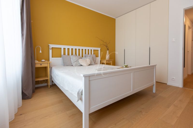 Bedroom in a 2-room apartment with wood-patterned flooring, yellow wall, white bed.