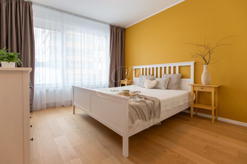 A bedroom in a two-room apartment with a wooden floor decor and a yellow wall.