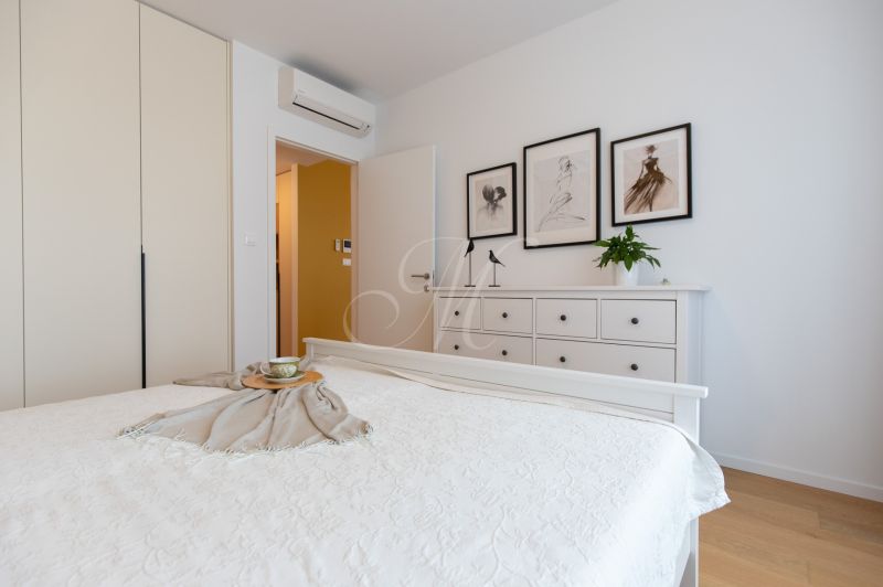 A bedroom in a two-room apartment with white furniture and a wooden decor floor.
