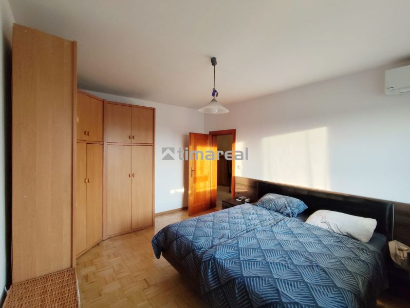 Bedroom in a two-room apartment with a bed, wardrobe, and wooden decor flooring.