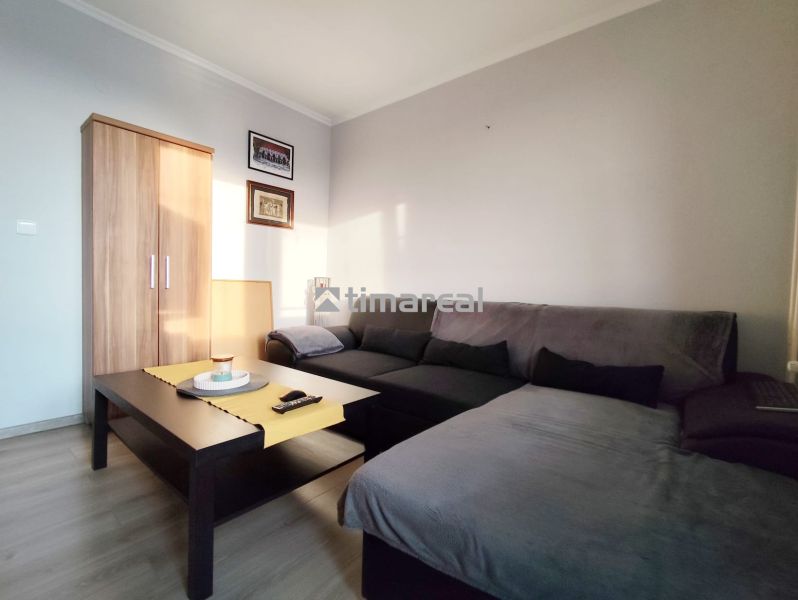 Living area of a 2-room apartment with a sofa, table, and wardrobe, floor with wooden decor.