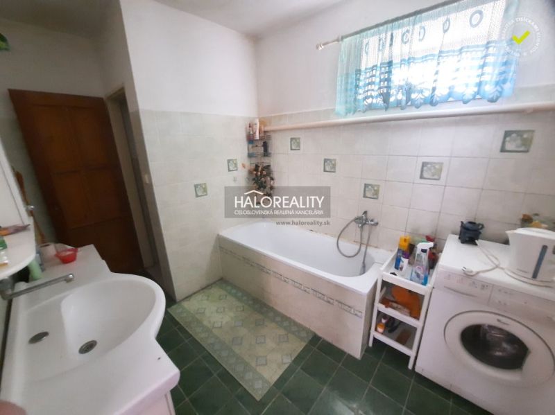 A bathroom in a family house with green tiles, a bathtub, and a washing machine.