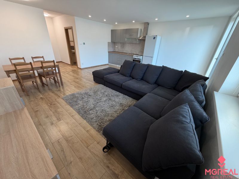 Living room with a dark sofa, dining table, and wooden decor flooring.