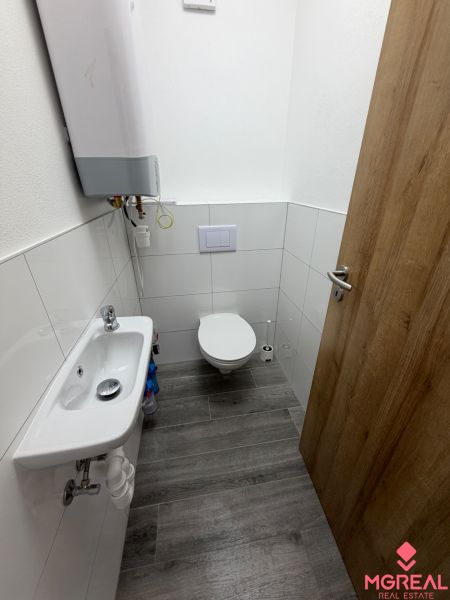 A toilet in a 3-room apartment with a wooden decor floor, small sink.