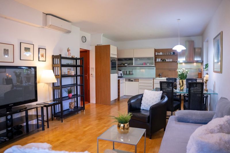 Living room in a 3-room apartment with a wooden decor floor, kitchenette, and dining table.