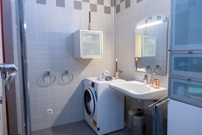 A bathroom with a washing machine, a sink, and gray tiles in a 3-room apartment.