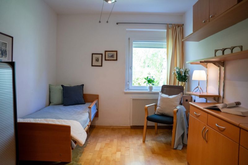 A room in a 3-room apartment with a bed, a wooden-decor floor, and a table with a lamp.