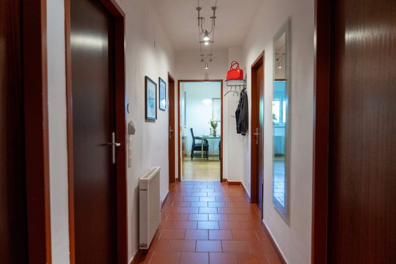 A hallway in a 3-room apartment with tiles leads to a room with flowers on the table.