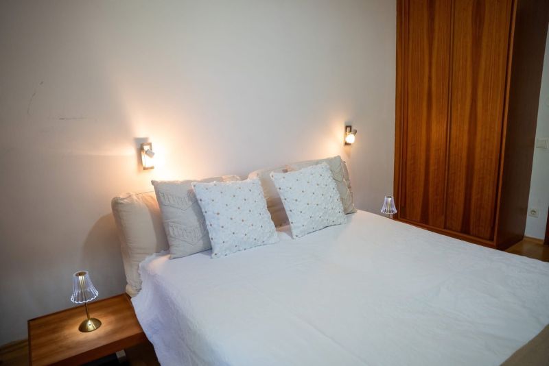 A bedroom in a 3-room apartment with a bed, pillows, and a wooden wardrobe.