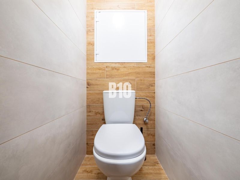 A toilet with ceramic tiles and a wooden decor floor in a studio apartment.