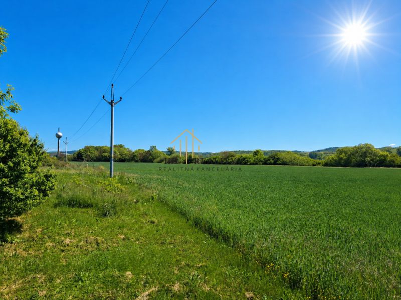 Záhorce, Land - residential: Green field with electric poles and surrounding forest.