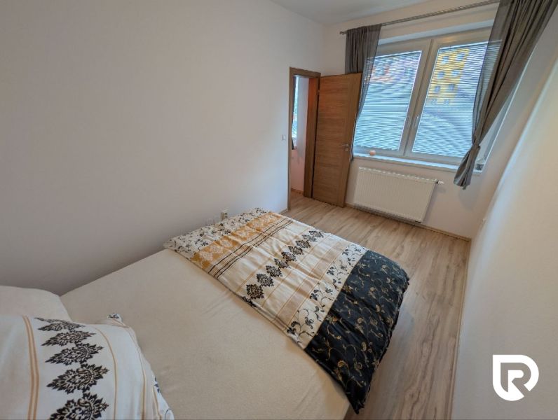 Bedroom with wood-patterned flooring in a 2-room apartment, bed and window with blinds.