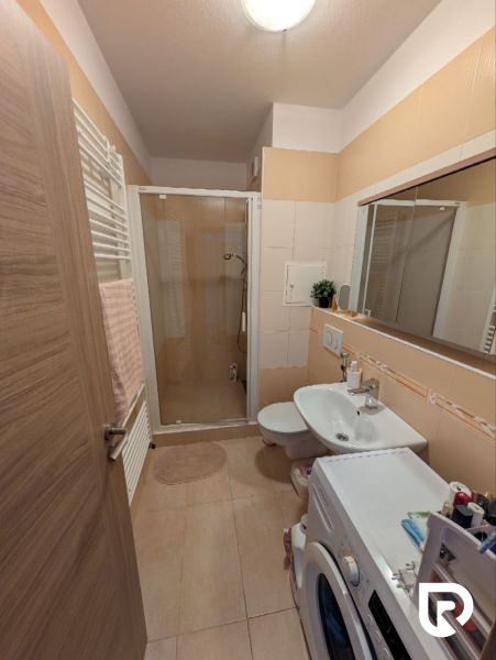 Bathroom in a 2-room apartment with a sink, shower, and washing machine, tiles in a beige shade.